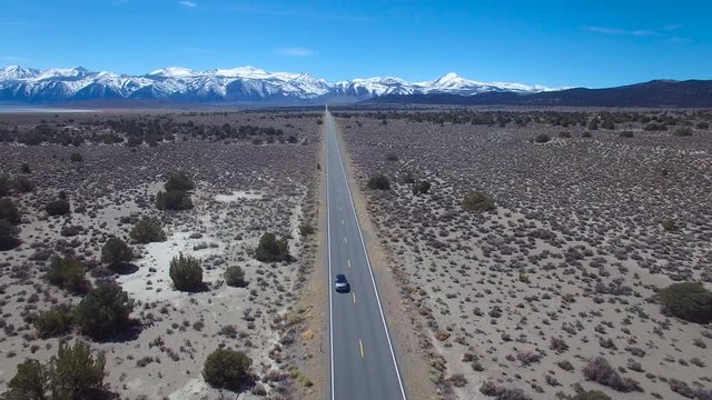 Aerial above a 4WD traveling on a paved road in the Mojave Desert with the Sierra Nevada mountains distant.