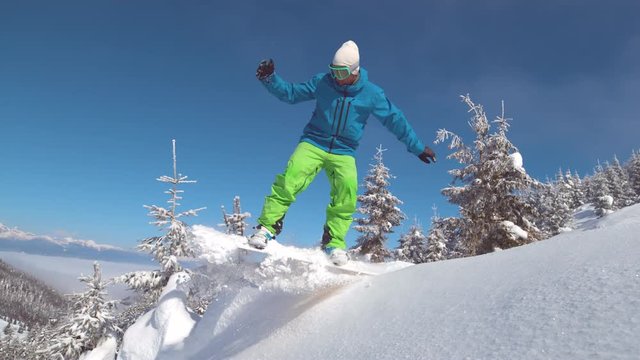 SUPER SLOW MOTION, CLOSE UP: Professional snowboarder rides down a perfect snowy hill and jumps high in the air. Extreme rider on snowboard jumps off a snow covered ledge on a beautiful winter day.
