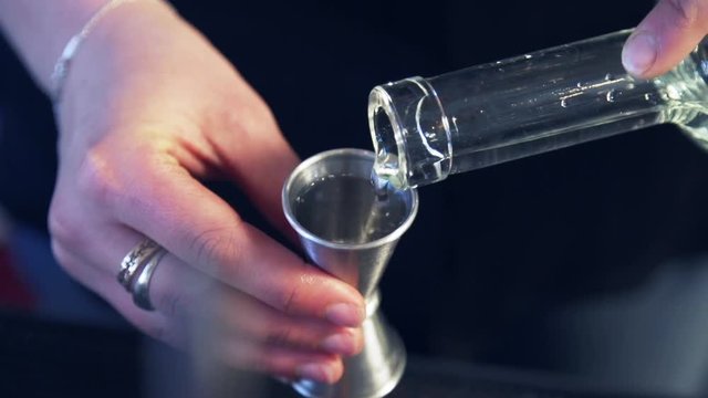 Clear alcohol poured into metal shot glass by bartender