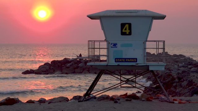 A sunset behind a lifeguard station along a California beach.