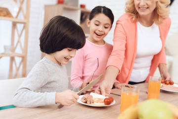 Little grandson with sister watching at eggs with sausages and tomatos on plate.