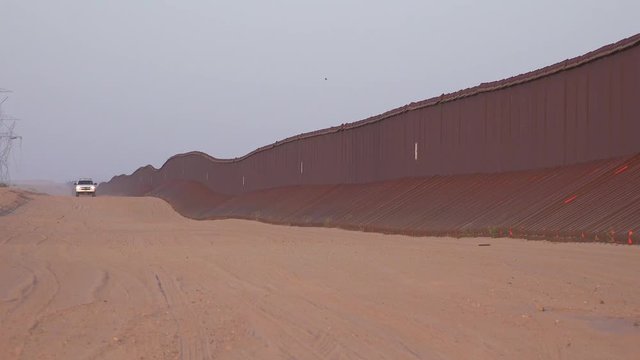 Border patrol vehicle moves slowly near the border wall at the US Mexico border at Imperial sand dunes, California.