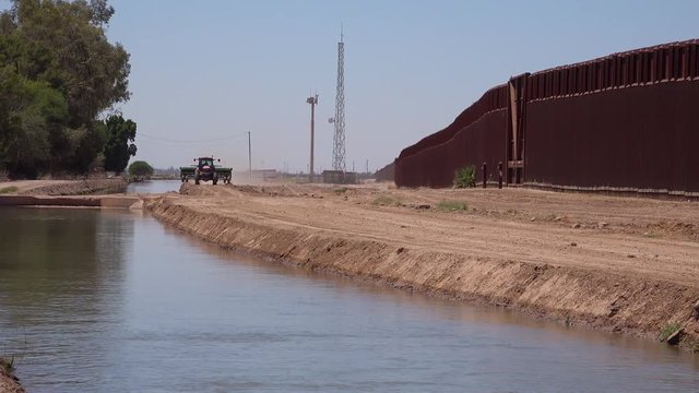 A farmers tractor follows a tributary of the Colorado River as it flows along the border wall between the US and Mexico.