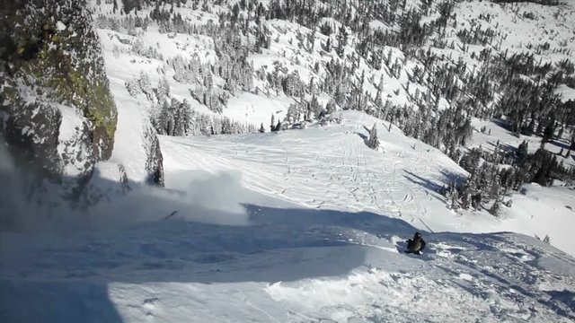A skier jumps off the side of a mountain, and another person sits below.