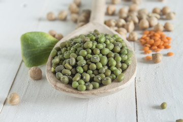 dry green grains masha in a spoon and other legumes on a table