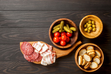 Ingredients for making tapas or bruschetta. Crusty bread, ham ,  tomatoes, olives on plates over dark texture background. Top view
