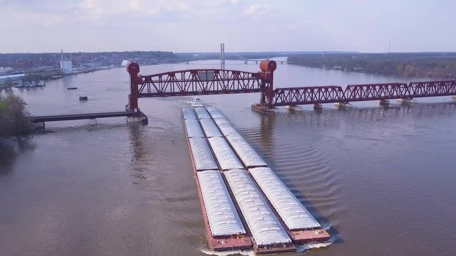 A beautiful aerial of a barge traveling under a steel drawbridge on the Mississippi River.