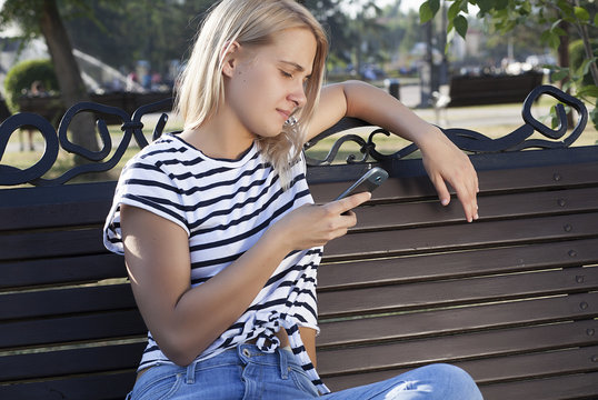 young beautiful blonde girl talking on mobile phone and smiling, talking on phone in park