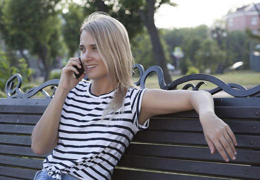 young beautiful blonde girl talking on mobile phone and smiling, talking on phone in park