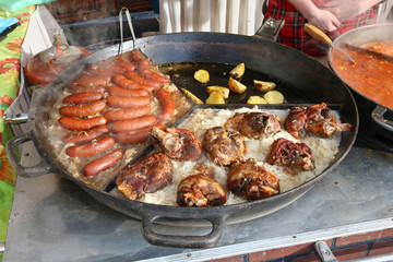 Fast street-food - smoked pork sausages, chicken legs  and stewed cabbage with popato in big frying pan.