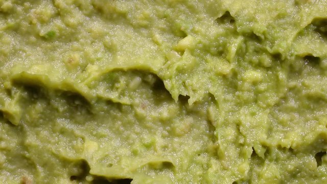Extreme closeup top view of avocado smash rotating in 4K. Traditional tasty sauce guacamole.
