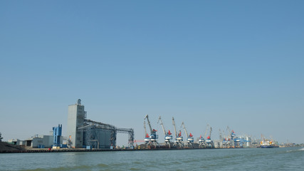 Fototapeta premium river port with cranes and industrial buildings in summer against a blue clear sky view from the water