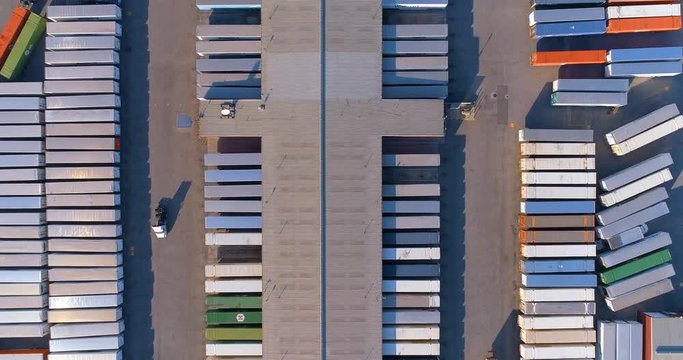 Large distribution center filled with shipping containers and 18 wheeler semi tractor trailer trucks moving inventory containers.