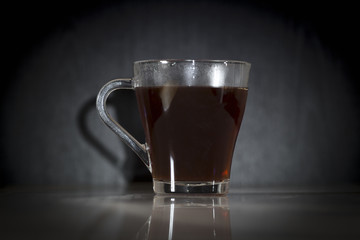 A glass with hot soaring tea on a black background.