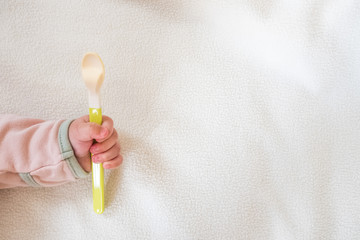 Baby hand hold tiny spoon on white blanket background : concept for baby food