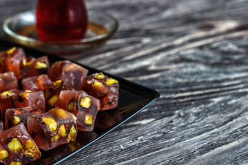 Oriental sweets with different nuts a glass of tea and a spoon. Eastern sweets. Traditional Turkish delight (Rahat lokum) on a wooden background. View from above.