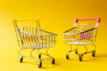 Close up of two supermarket grocery push carts for shopping with wheels and yellow and pink plastic elements on handle isolated on yellow background. Concept of shopping. Copy space for advertisement