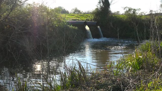 Contaminated water is dumped into a waterway through industrial pipes.