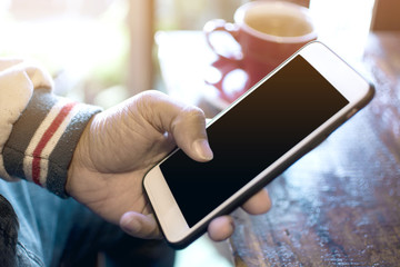 Close up man using smart phone, male holding black screen mobile phone with blurred cup of coffee in the cafe
