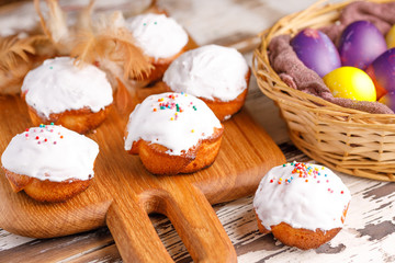 Fresh pastry with sugar icing on a wooden board and basket with painted eggs.