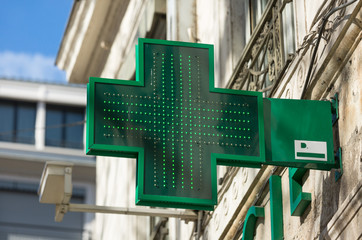 Closeup of a green pharmacy sign outside a pharmacy store in France.