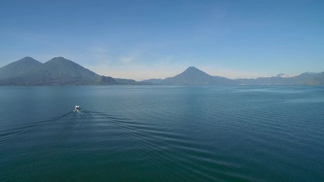 Aerial over a boat on Lake Amatitlan in Guatemala reveals the Pacaya Volcano in the distance.