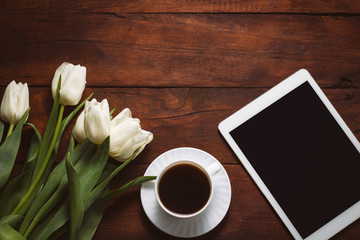 White Tulips, a cup of coffee and a tablet on a dark wooden background. Concept of Spring. Flat lay, top view