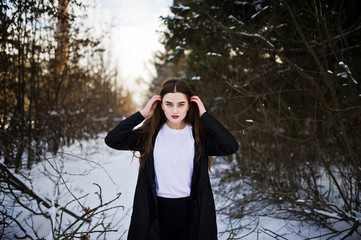 Fashionable long legs brunette model in long black cloak posed outdoor at winter day.