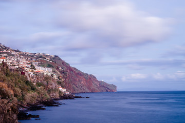 Small mountain houses located on a coastline in front of the ocean during twilight blue hour in Funchal, Madeira, Portugal