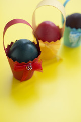 Colorful eastern eggs warped in paper cups on yellow background. Selective focus