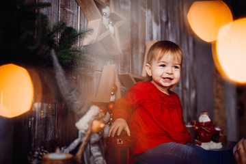 Fototapeta na wymiar Smiling little girl sits on the shelf between beautiful Christmas decorations