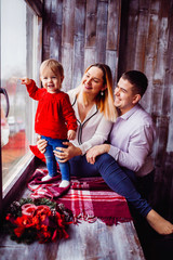 Mom and dad play with little child while she stands on the windowsill