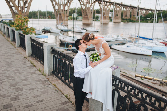 Young bride and groom kiss on the beautiful embankment. International wedding of Asian and European.