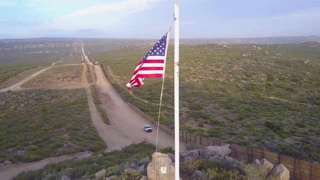 The American flag flies over the U.S. Mexico border wall in the California desert as a border patrol vehicle passes below.