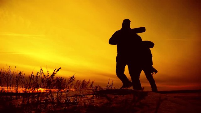 Silhouettes of two hikers with backpacks enjoying sunset view from top of a mountain