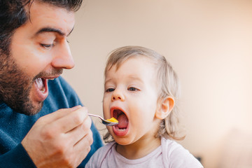 Father feeding toddler baby infant with spoon and mango