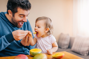 Father feeding toddler baby infant with spoon and mango - Powered by Adobe