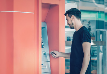 Fototapeta na wymiar Young man using credit card for cash withdrawal in ATM machine