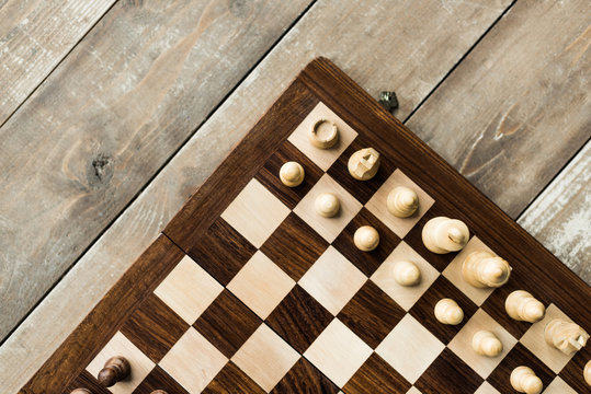 Cropped view of chess baord with chess pieces on rustic wooden surface