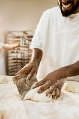 cropped shot of african american baker cutting dough with dough knife
