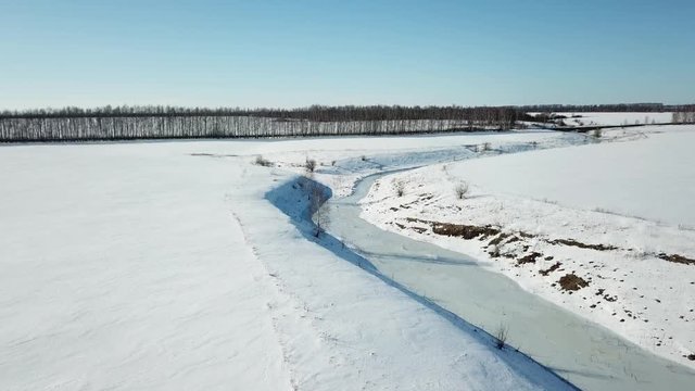 Flying over small frozen river. Ice and snow. Aerial view landscape