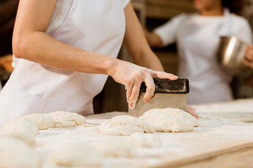 cropped shot of female baker cutting dough with dough knife