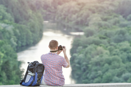 Man takes pictures from a hill. Forest and river below