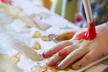 A little girl paints with brush and paints on a piece of paper