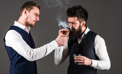 Assistant helping his boss light cigar with lighter. Luxury leisure