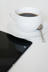 Black tablet pc with cup of coffee on the table.
