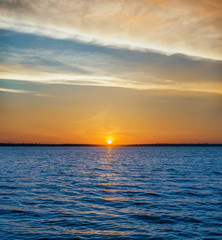 blue dark water in river and orange sunset in clouds