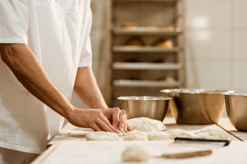 cropped shot of baker preparing raw dough on baking manufacture