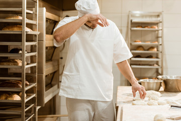 exhausted baker working with raw dough at on baking manufacture and wiping sweat
