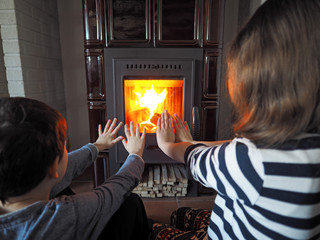 little girl and little boy warm up by the fireplace